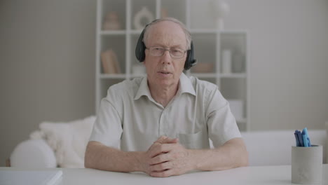 Ein-älterer-Mann-Mit-Kopfhörern-Blickt-In-Die-Kamera,-Begrüßt-Das-Online-Publikum-Und-Beginnt-Mit-Dem-Lern-Webinar